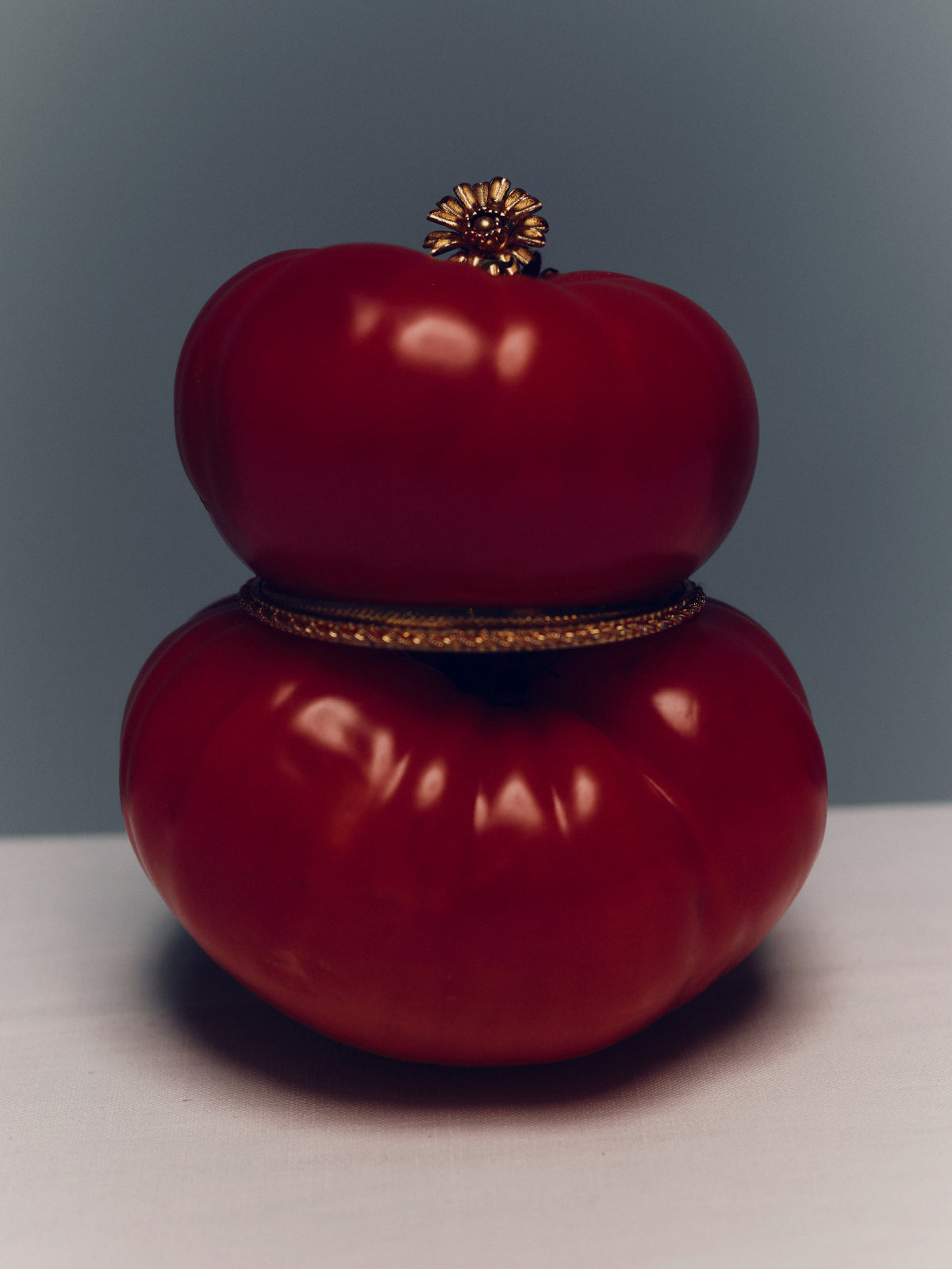 Red decorative tomato with gold accents on a gray background